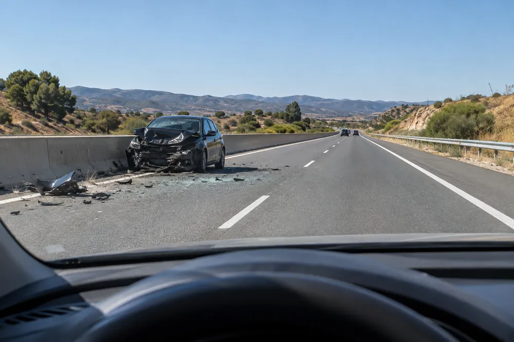 Turismo accidentado contra la mediana de una autovía, con restos en la calzada, visto desde un coche que llega.