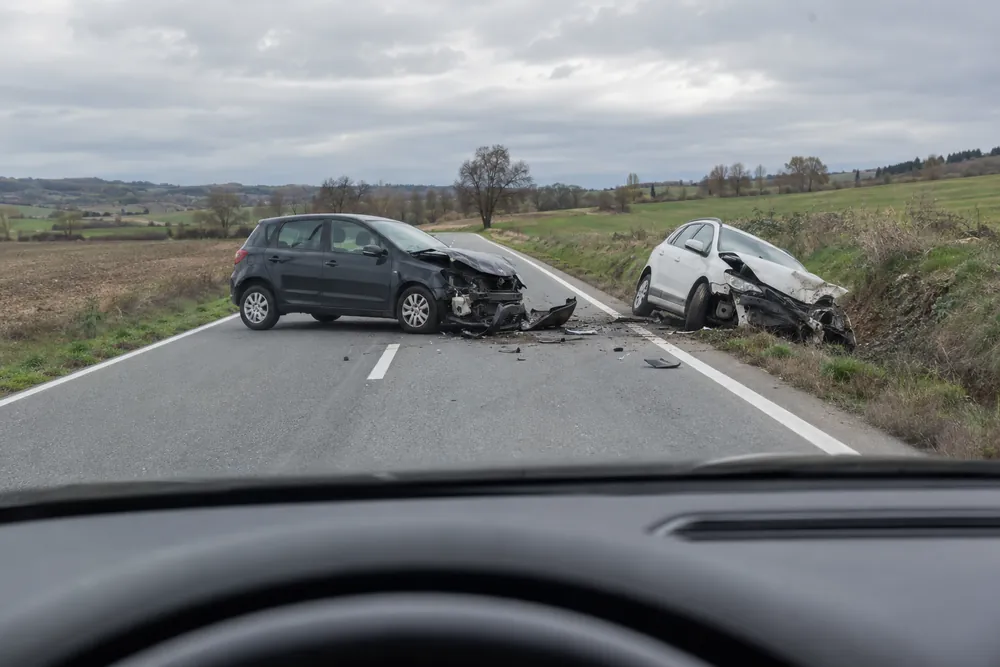 Dos turismos accidentados en una carretera convencional, vistos desde el coche que llega.