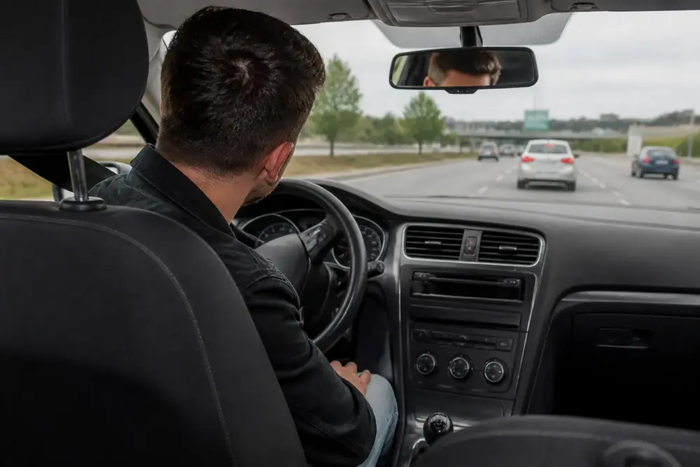 Conductor al volante en autovía visto desde el asiento trasero, con el retrovisor interior a la vista