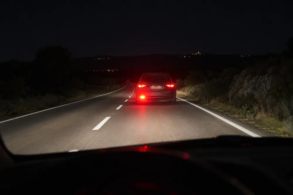 Turismo que circula delante con un piloto antiniebla trasero muy brillante en una noche despejada.