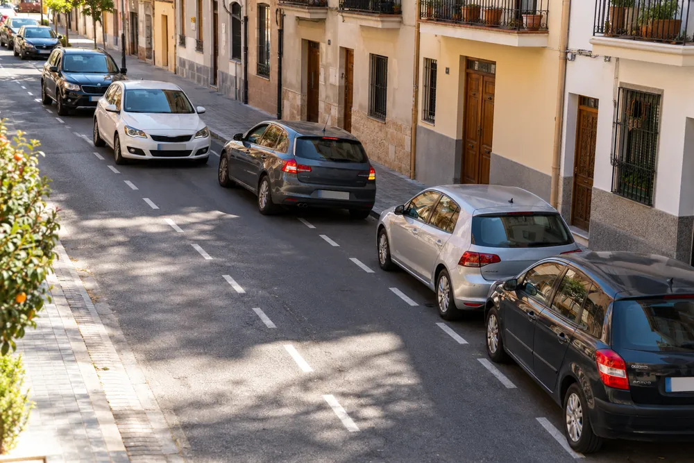 Turismo maniobrando para estacionar en línea mientras otros coches esperan detrás.