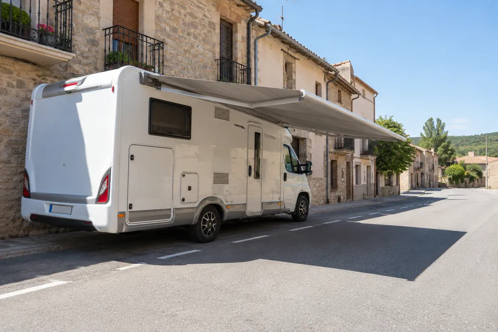 Autocaravana estacionada junto a una acera con el toldo desplegado fuera de su perímetro.