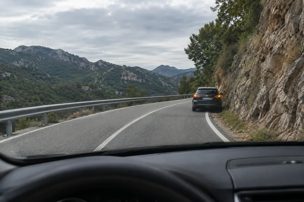 Turismo averiado detenido justo después de una curva cerrada sin visibilidad, visto desde el coche que la toma.