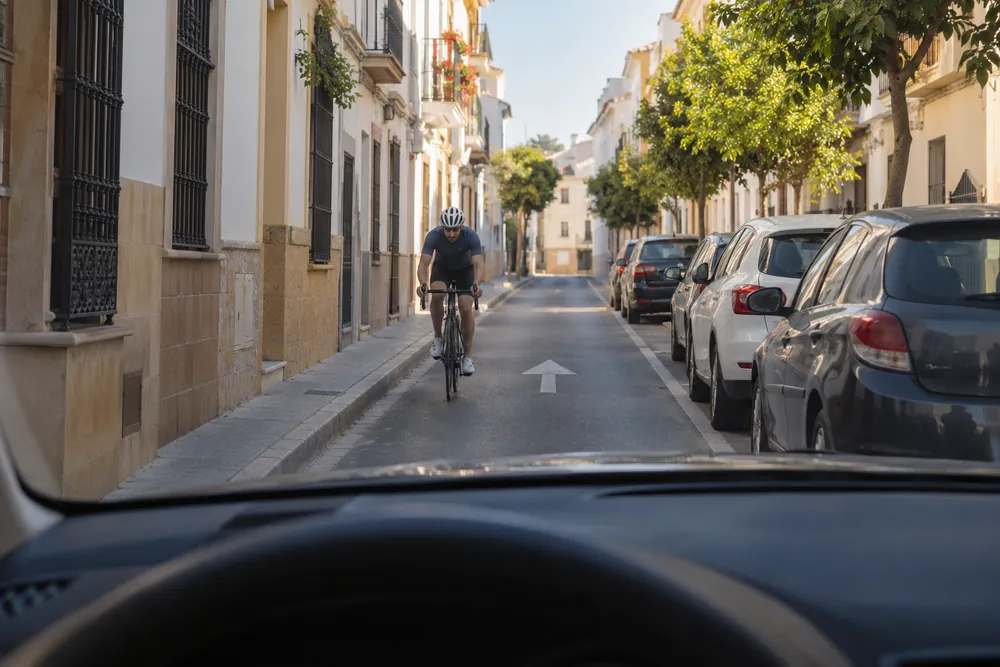 Ciclista que viene de frente por el mismo carril en una calle residencial estrecha de sentido único.