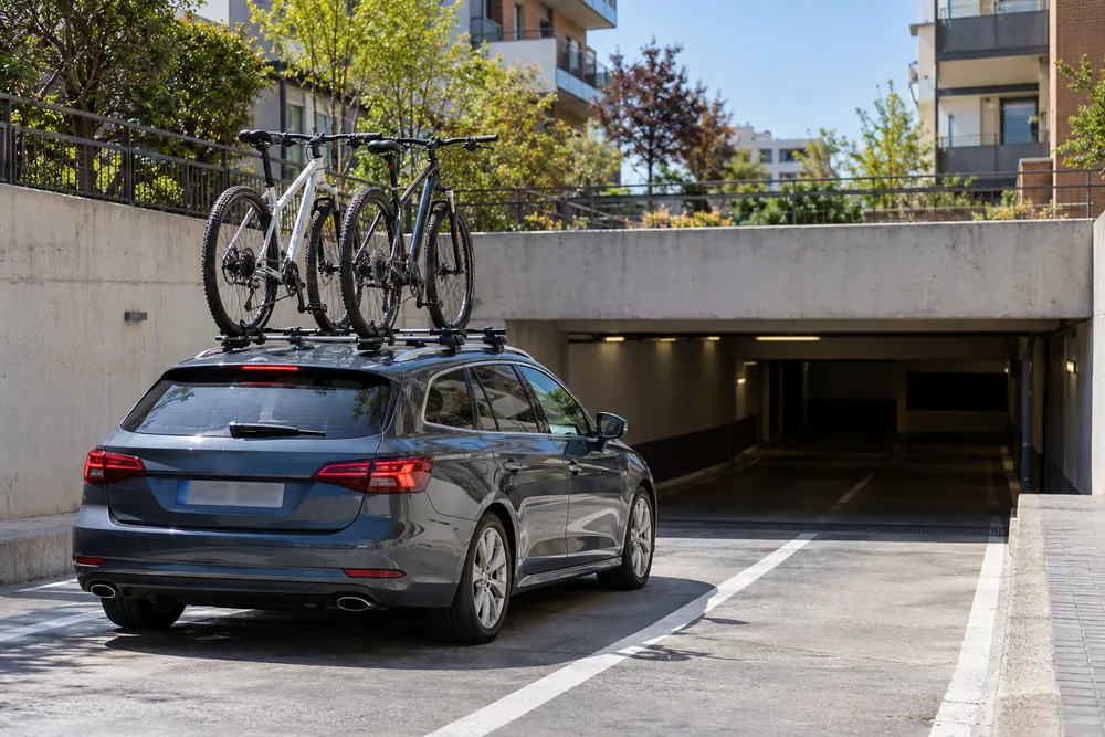 Turismo con dos bicicletas en el techo acercándose a la entrada de un aparcamiento subterráneo de techo bajo.