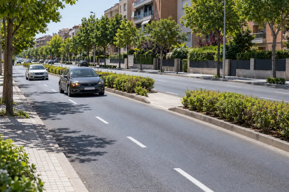 Turismo detenido en la abertura de la mediana de una avenida para cambiar de sentido, con otro coche acercándose por detrás.