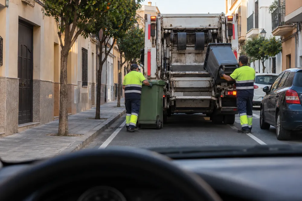 Camión de recogida de basura trabajando en una calle estrecha y cortando el paso.
