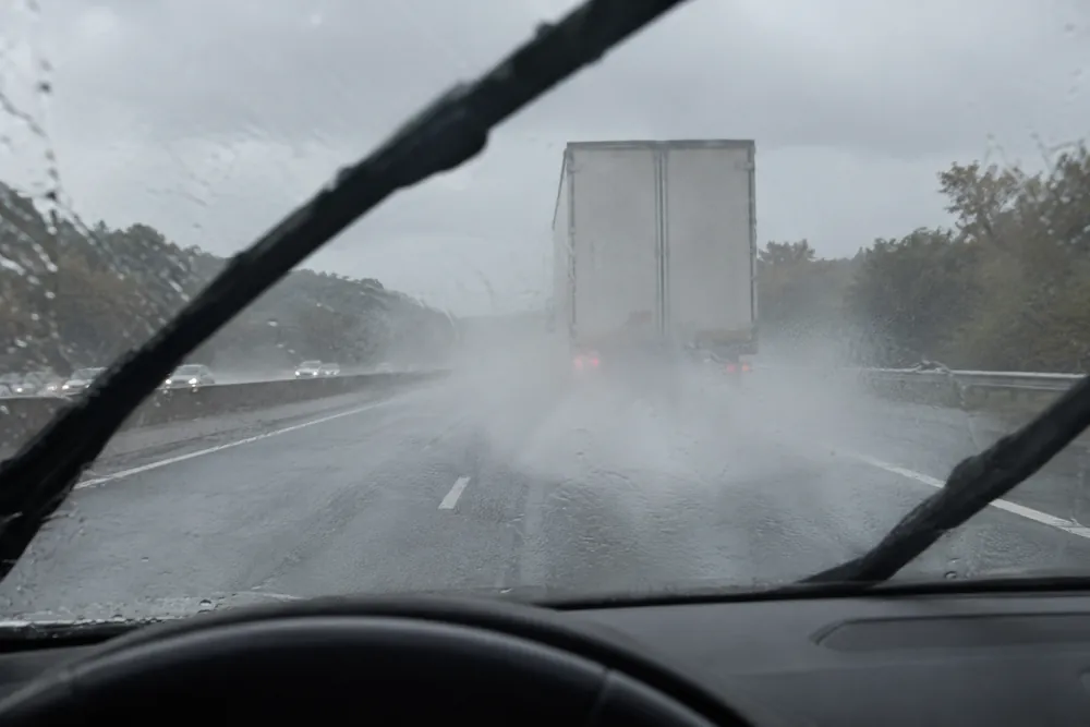 Camión que levanta una cortina de agua en una autovía mojada, visto desde el coche que va detrás.