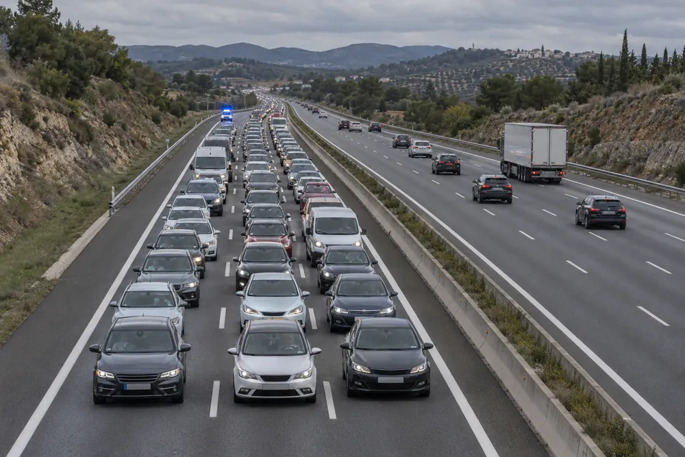 Autovía de tres carriles detenida por una retención, con un vehículo de emergencia acercándose por detrás.