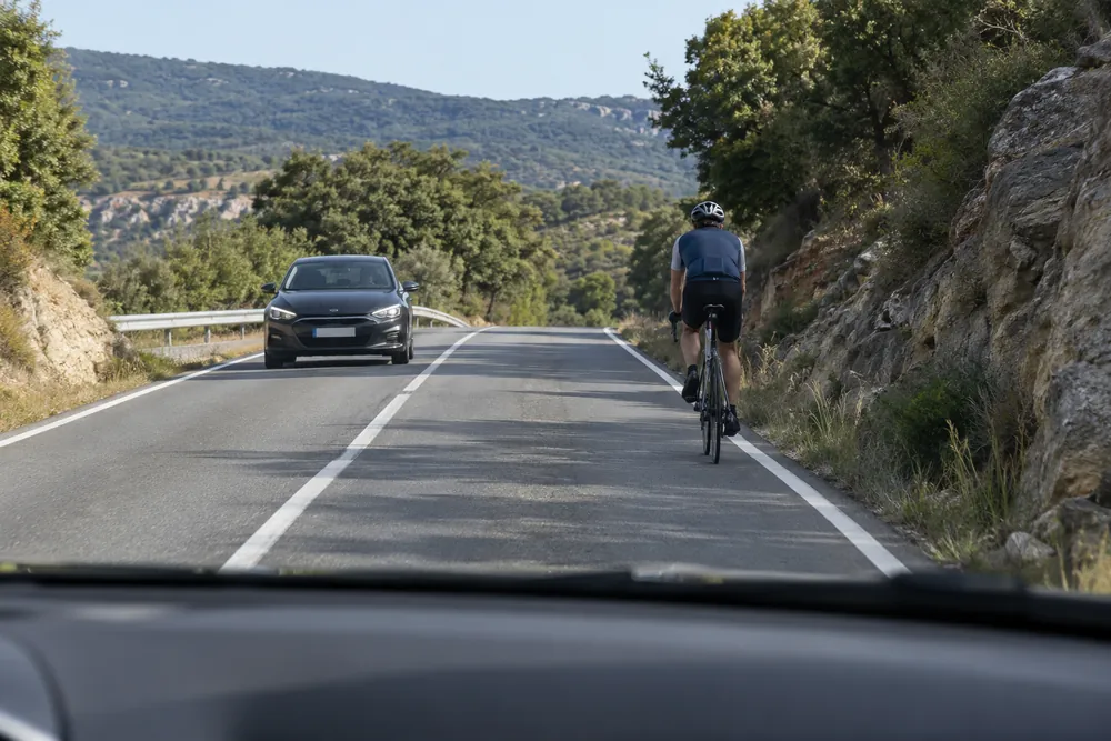 Ciclista delante y coche aproximándose por el sentido contrario.