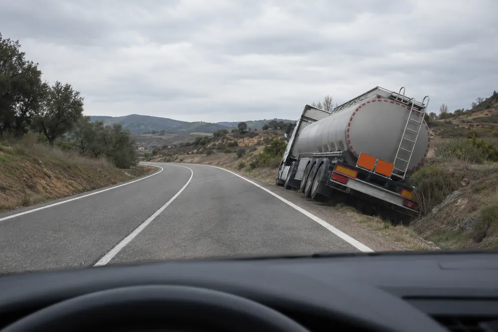 Camión cisterna con paneles naranjas detenido tras salirse de la calzada, visto desde un coche que se acerca.