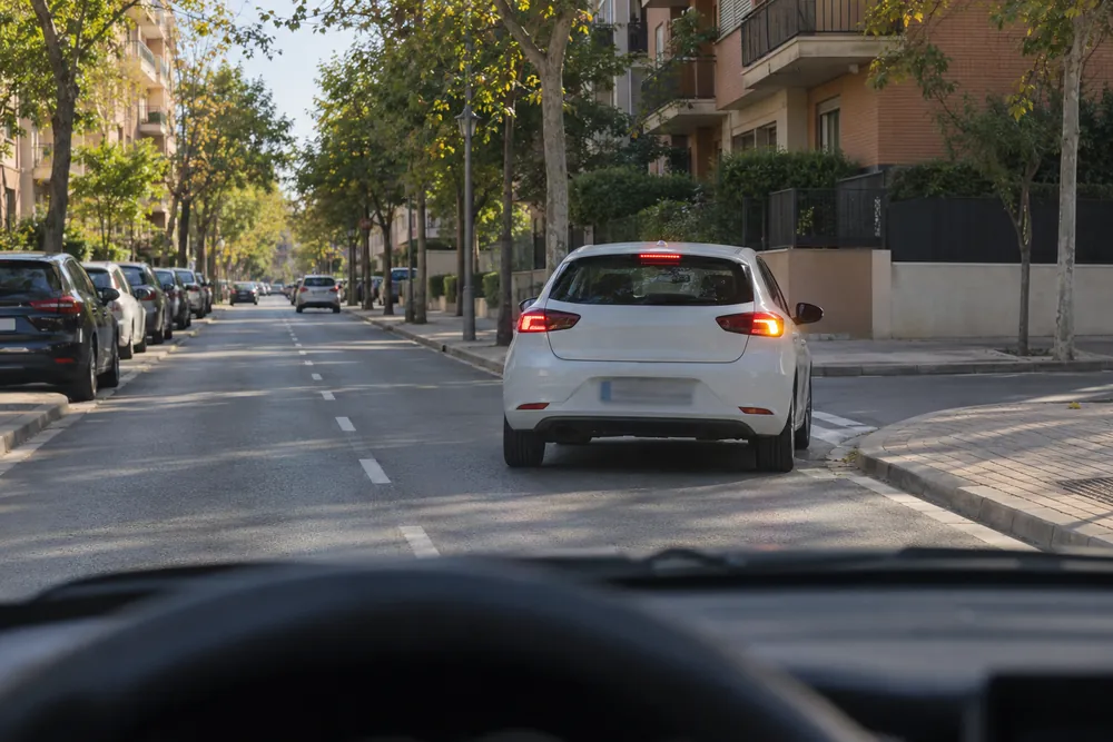 Turismo que reduce y lleva el intermitente derecho puesto para entrar en una calle, visto desde el coche de detrás.