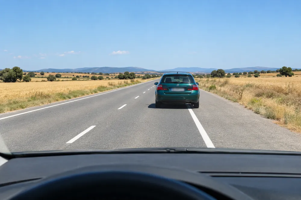 Turismo que se aparta al arcén ancho de una carretera convencional, visto desde el coche que viene detrás.