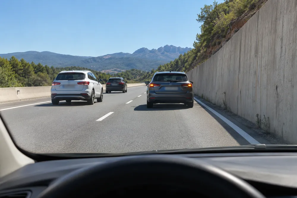 Turismo detenido en el carril derecho de una autovía sin arcén, con las luces de emergencia, visto desde el coche que se acerca.