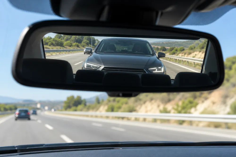 Turismo pegado detrás, visto en el retrovisor interior.