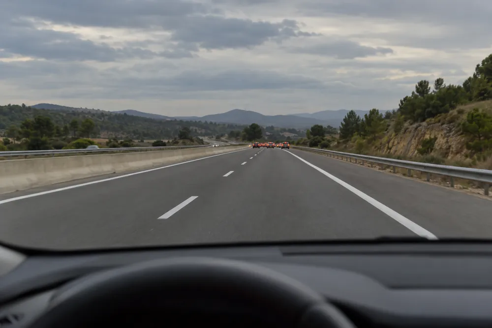 Cola de vehículos detenida a lo lejos en una autovía, con luces de freno y de emergencia encendidas.