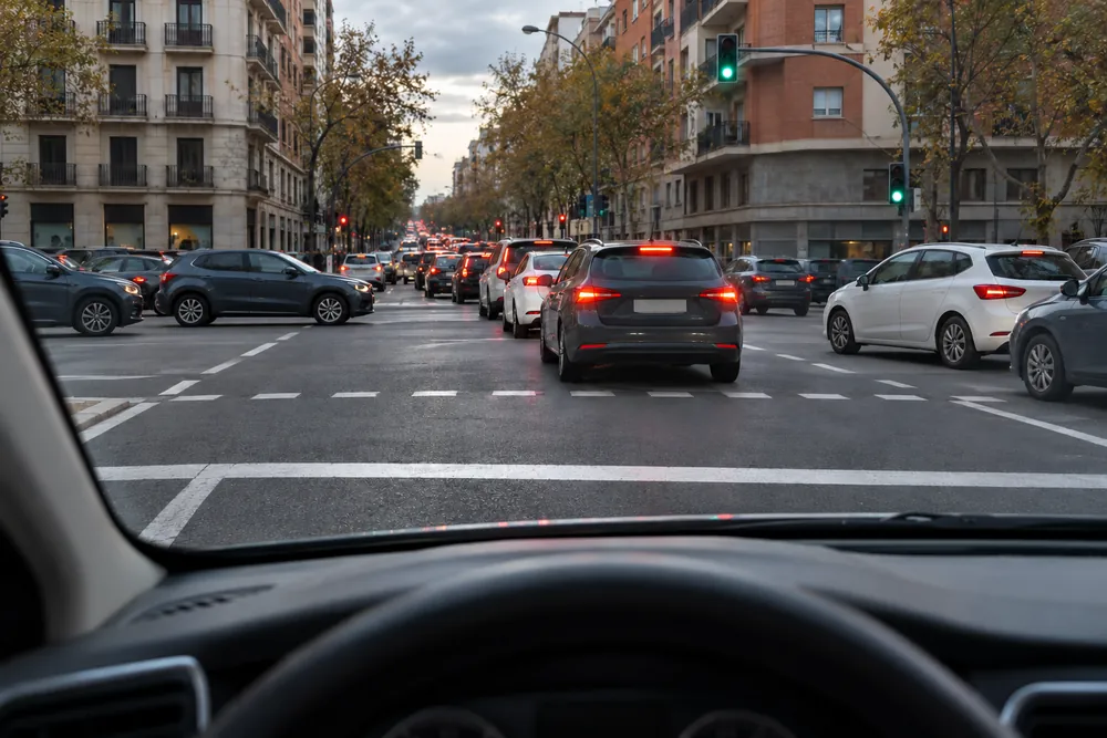 Semáforo en verde con la cola detenida dentro de la intersección, vista desde el coche que espera.