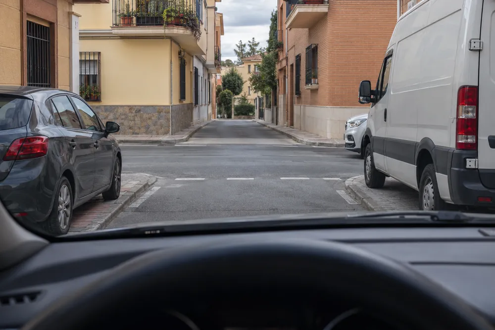 Cruce urbano con la visibilidad tapada por coches estacionados en la esquina.