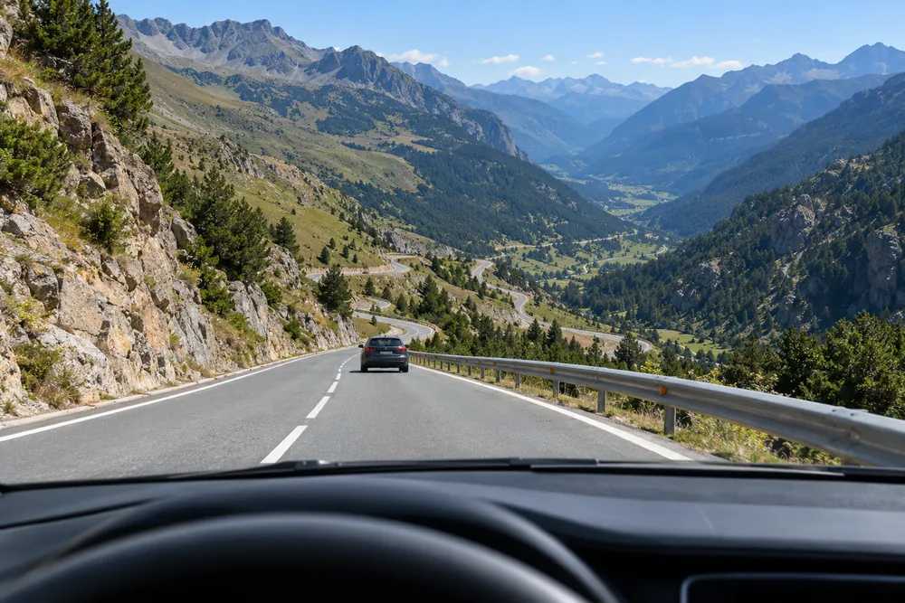 Bajada larga de un puerto de montaña vista desde el puesto de conducción, con otro vehículo por delante.