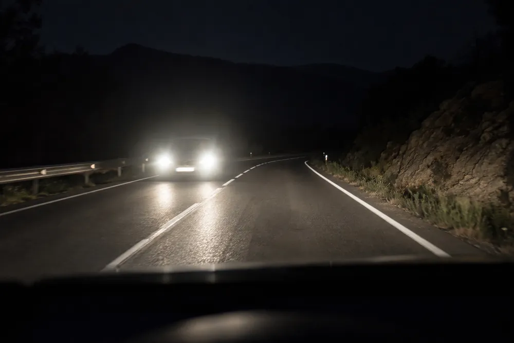 Faros de un coche que viene de frente en una carretera oscura.