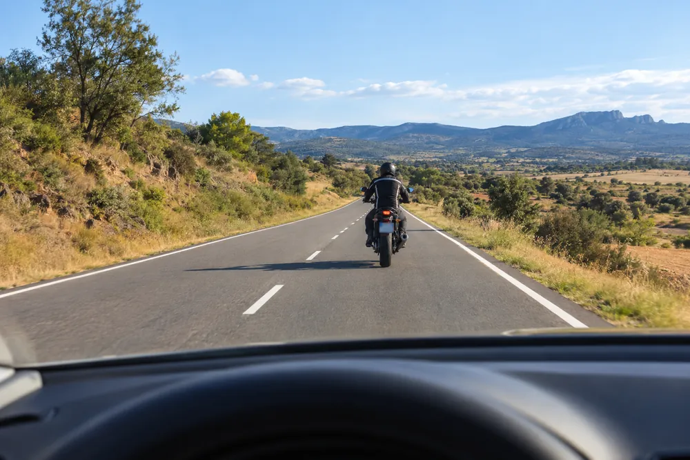 Turismo circulando detrás de una motocicleta en una carretera.