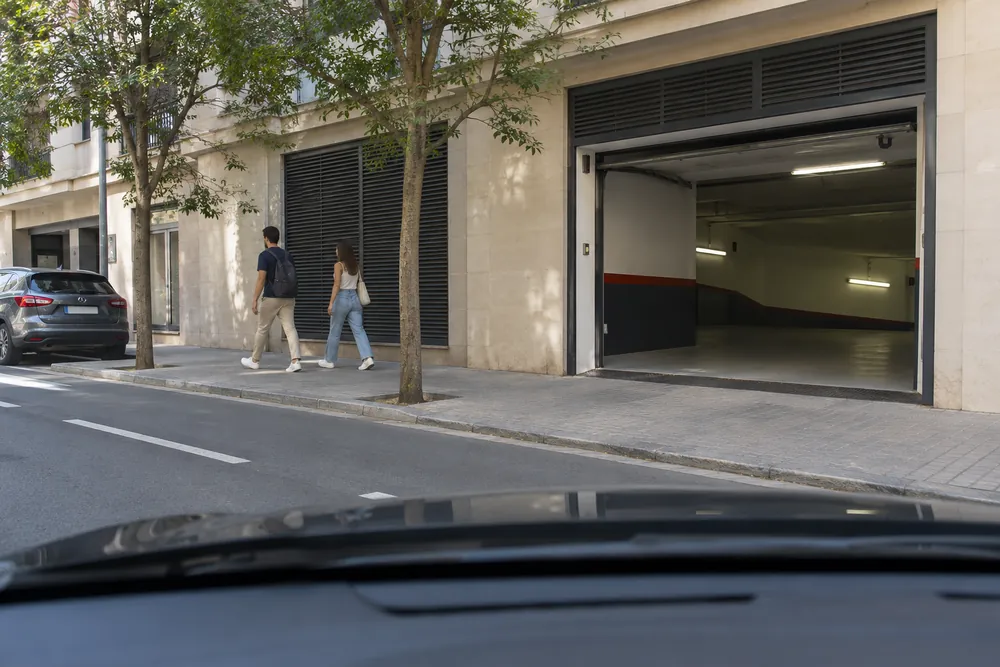 Entrada de garaje al otro lado de una acera por la que pasan peatones.
