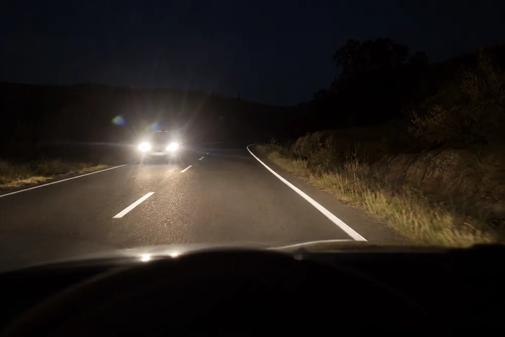 Faros de un vehículo que se acerca de frente de noche por una carretera sin iluminar.