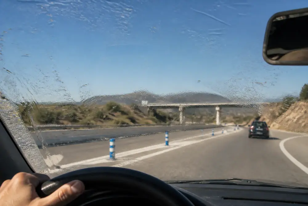 Parabrisas sucio a contraluz que reduce la visibilidad al conducir