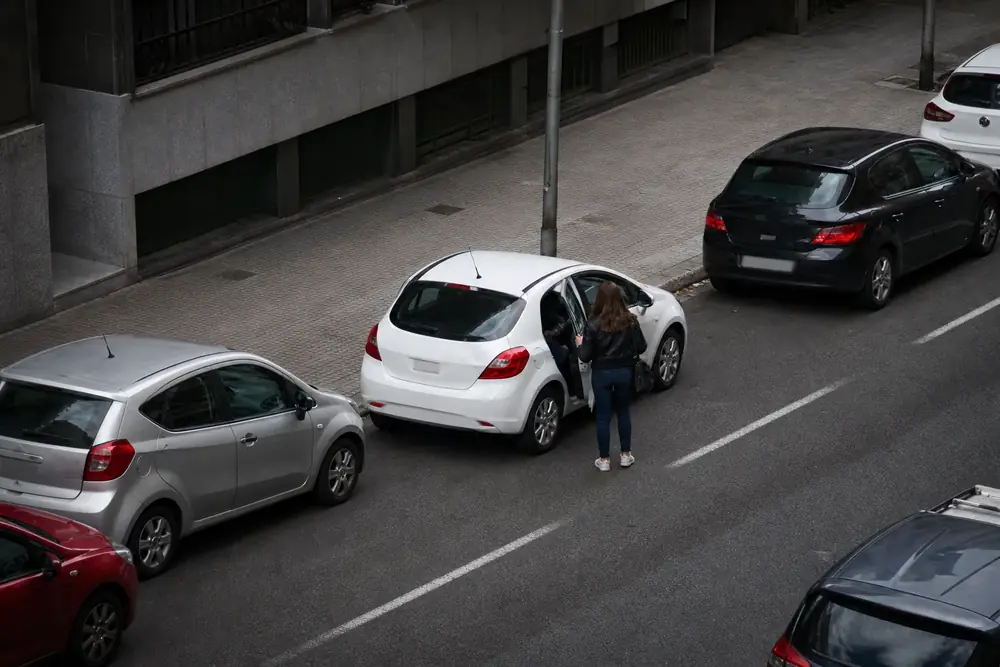 Persona apeándose del vehículo hacia la calzada entre coches aparcados