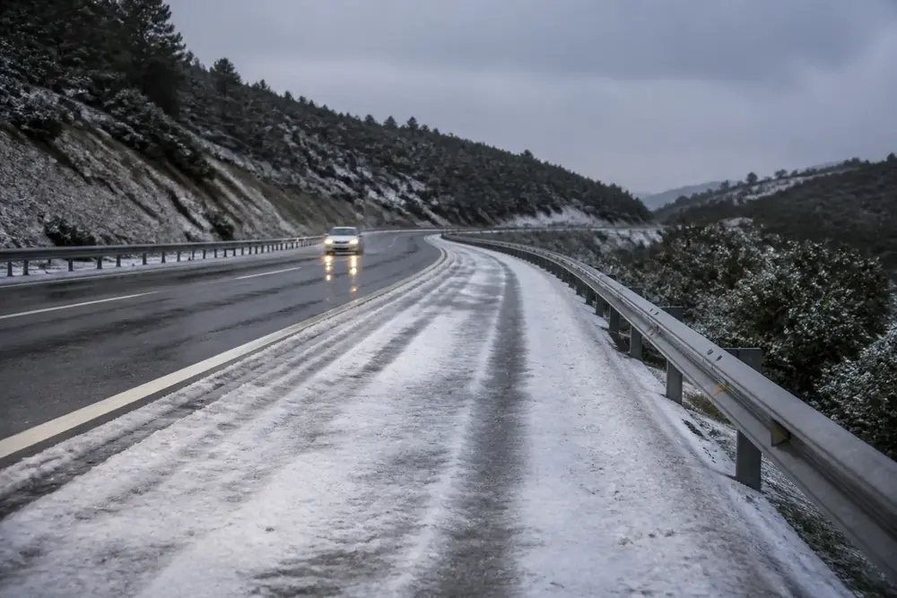 Carretera nevada con un vehículo circulando con las luces encendidas