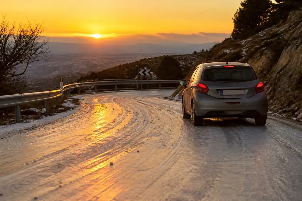 Turismo circulando por una carretera helada al atardecer