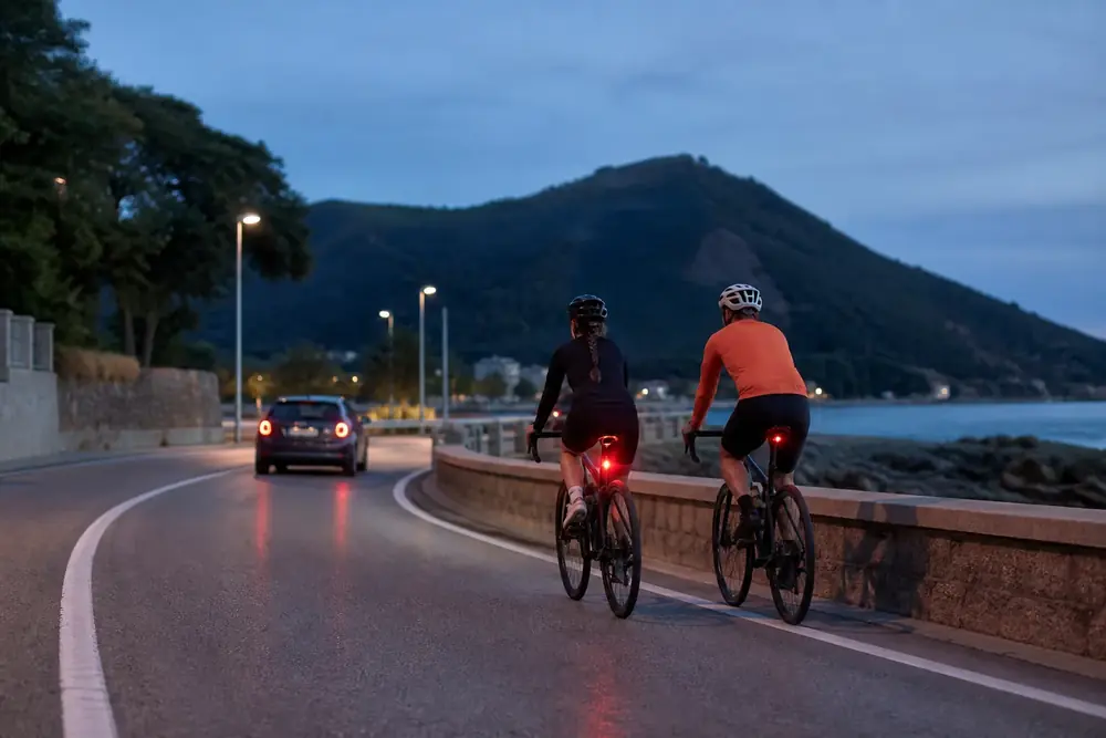 Dos ciclistas con luz trasera encendida circulando al anochecer