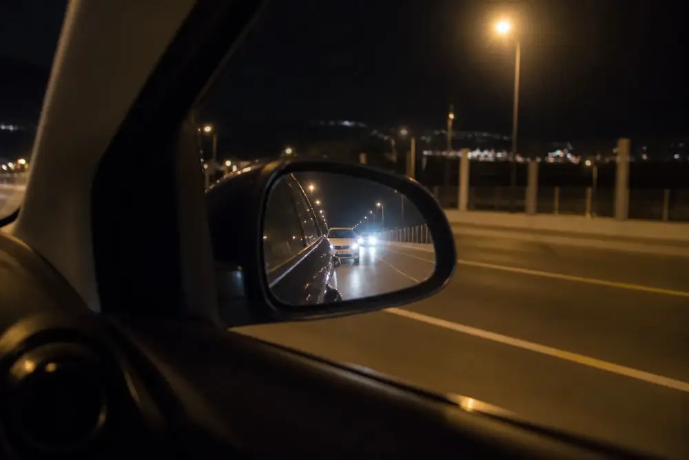 Faros de un vehículo que se acerca reflejados en el retrovisor de noche