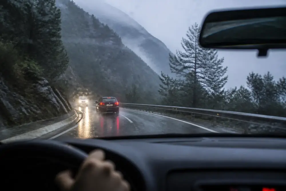 Carretera de montaña con lluvia y los vehículos con las luces encendidas