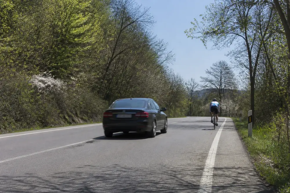 Turismo aproximándose por detrás a un ciclista en carretera