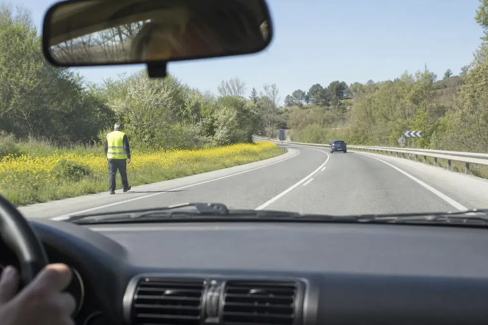 Peatón con chaleco reflectante en el arcén visto desde el coche