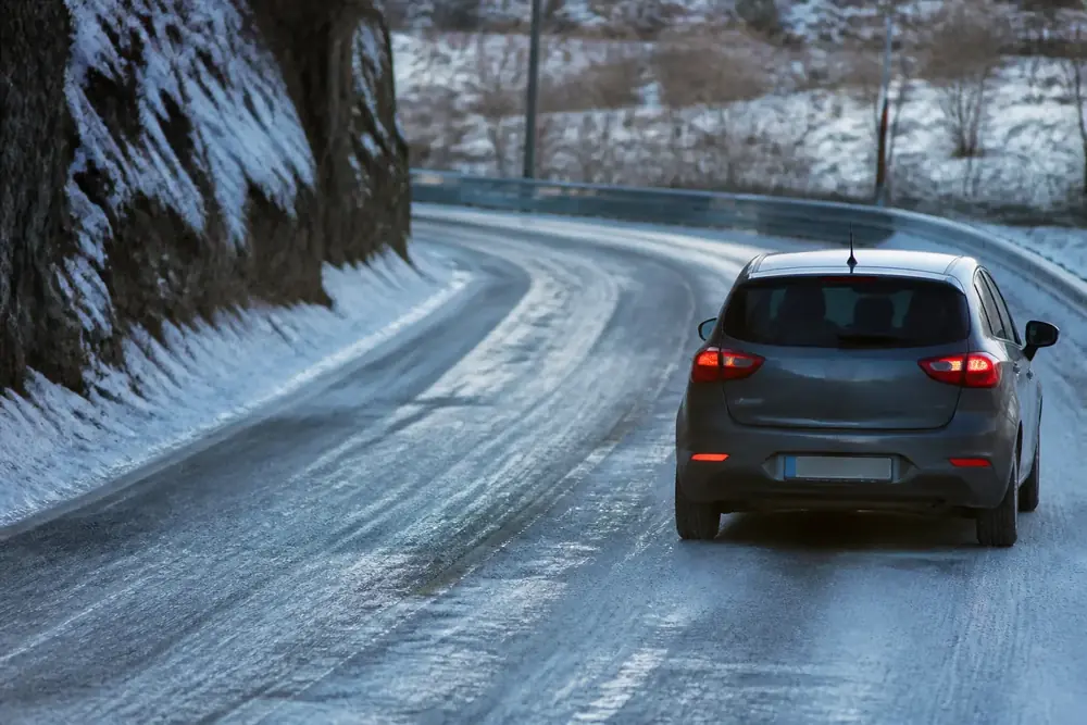 Vehículo circulando por una carretera helada con nieve en los márgenes