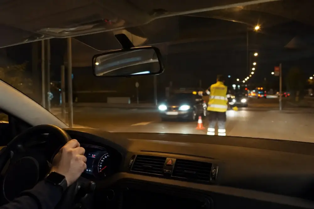 Agente con chaleco regulando el tráfico de noche, visto desde el volante