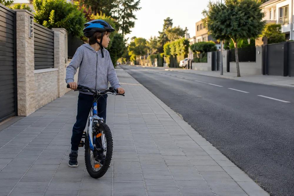 Niño con bicicleta en una acera amplia.