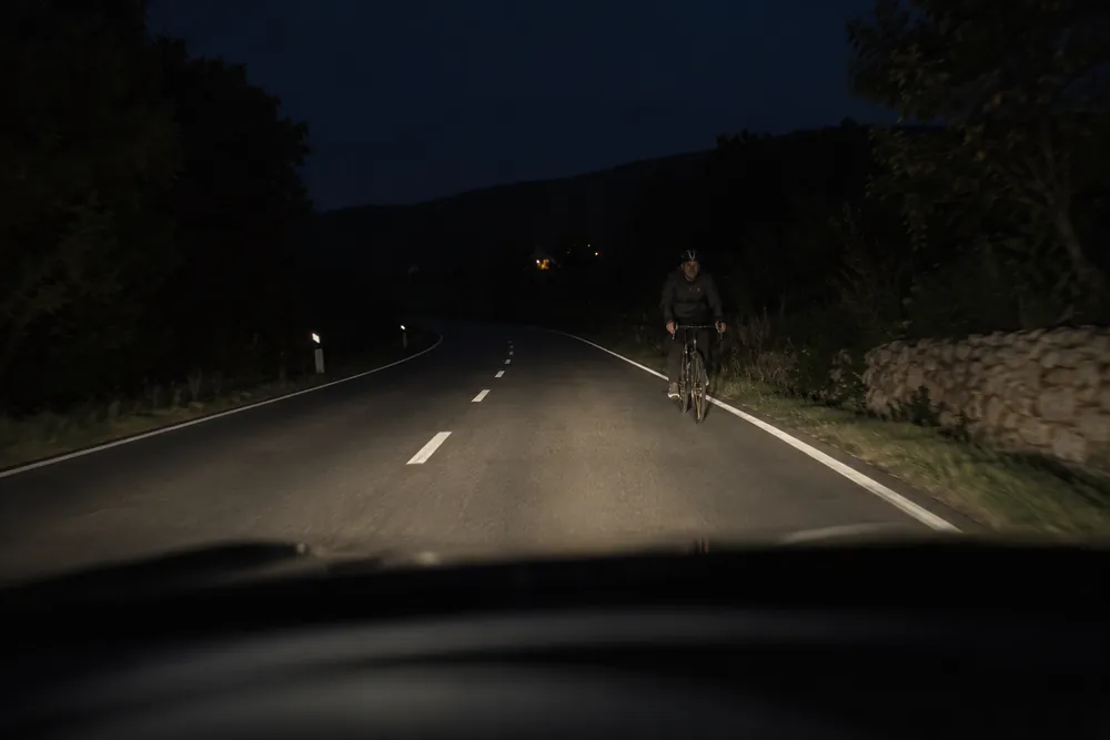 Ciclista que se aproxima de frente por una carretera oscura.