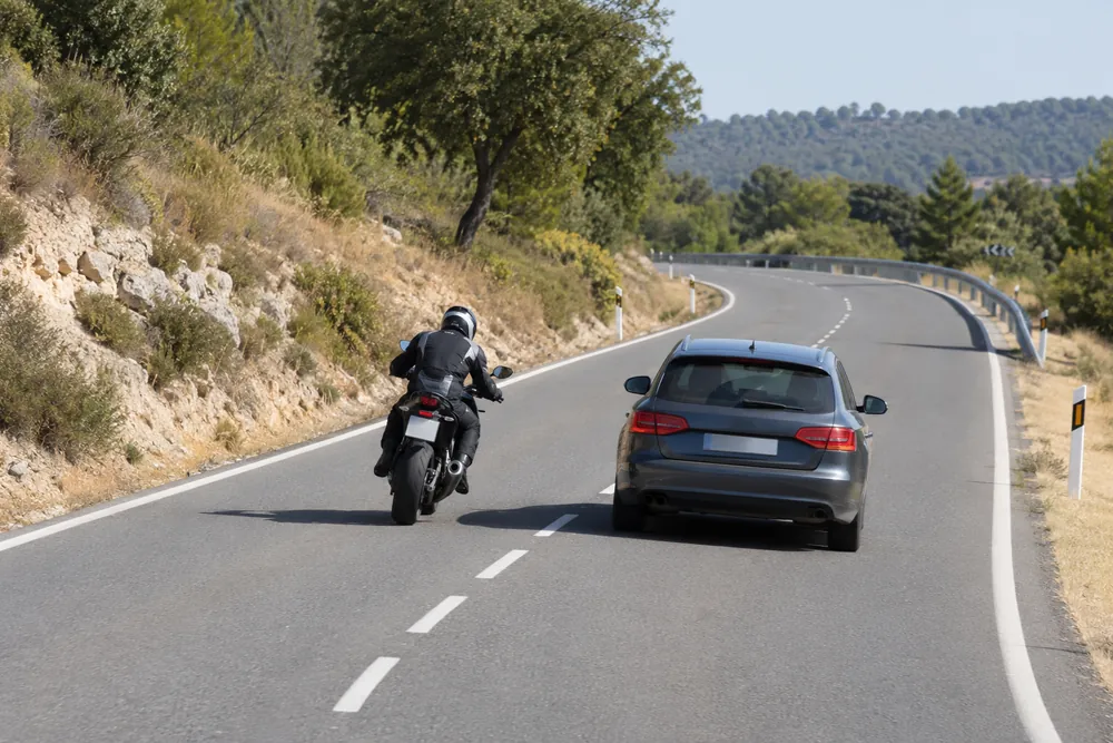 Motocicleta adelantando a un turismo en carretera convencional.