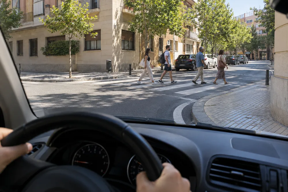 Peatones cruzando la calle a la que va a entrar un turismo que gira a la derecha.