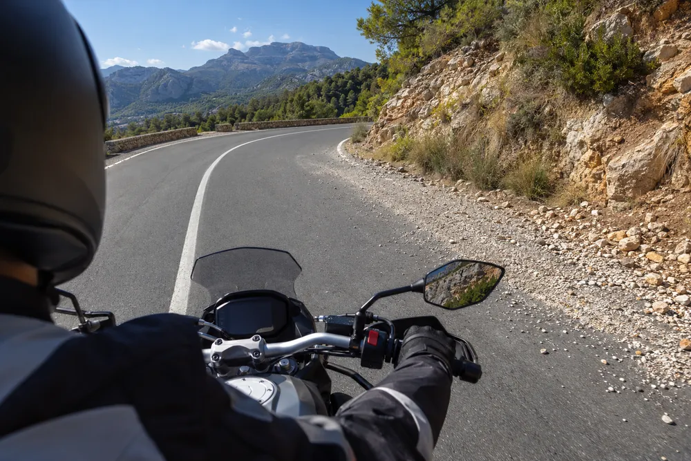 Curva de montaña con gravilla suelta en la trazada, vista por un motorista que se acerca.