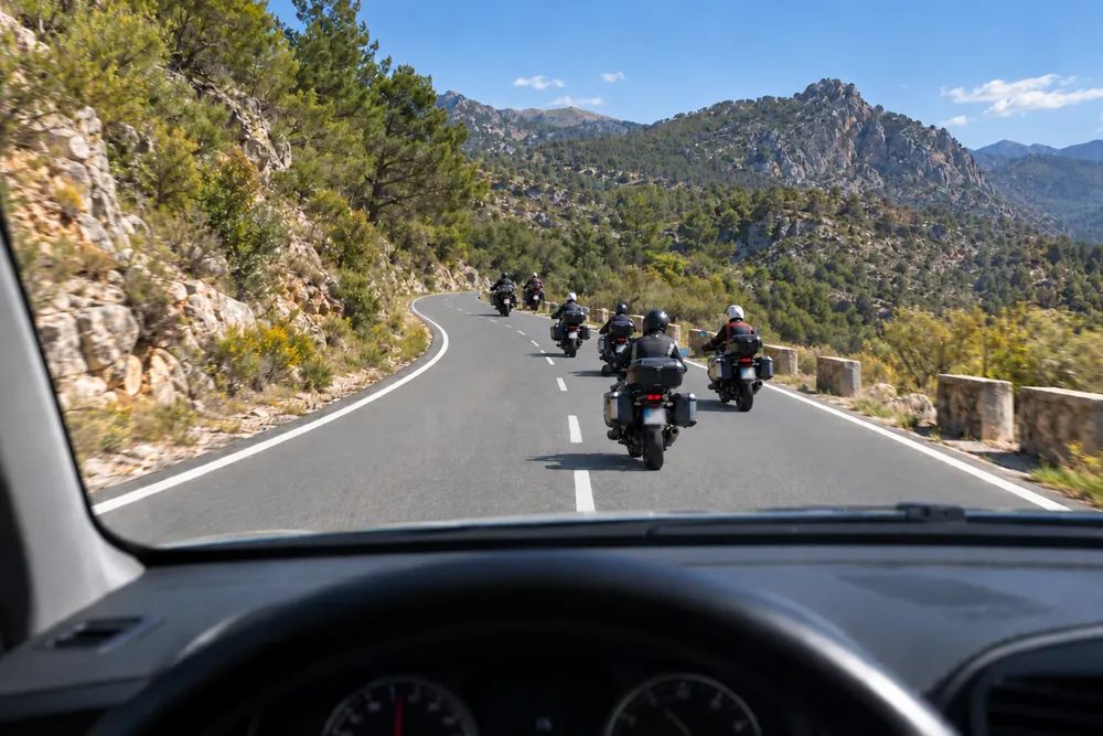 Grupo de motoristas circulando en formación escalonada por una carretera convencional, vistos desde el coche de detrás.