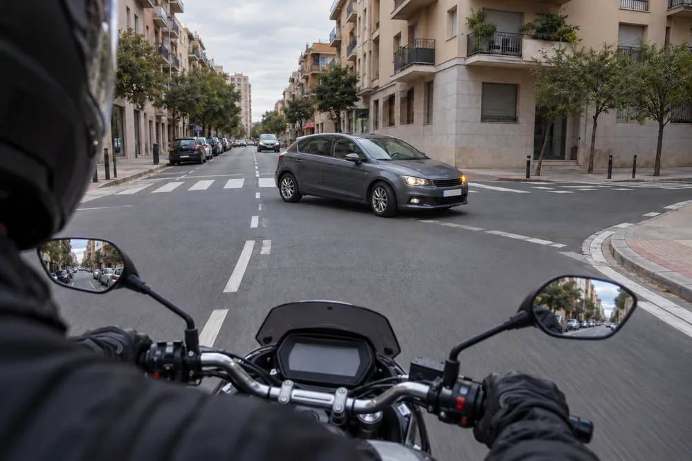 Turismo que gira a la izquierda cruzándose delante de una motocicleta en un cruce urbano.