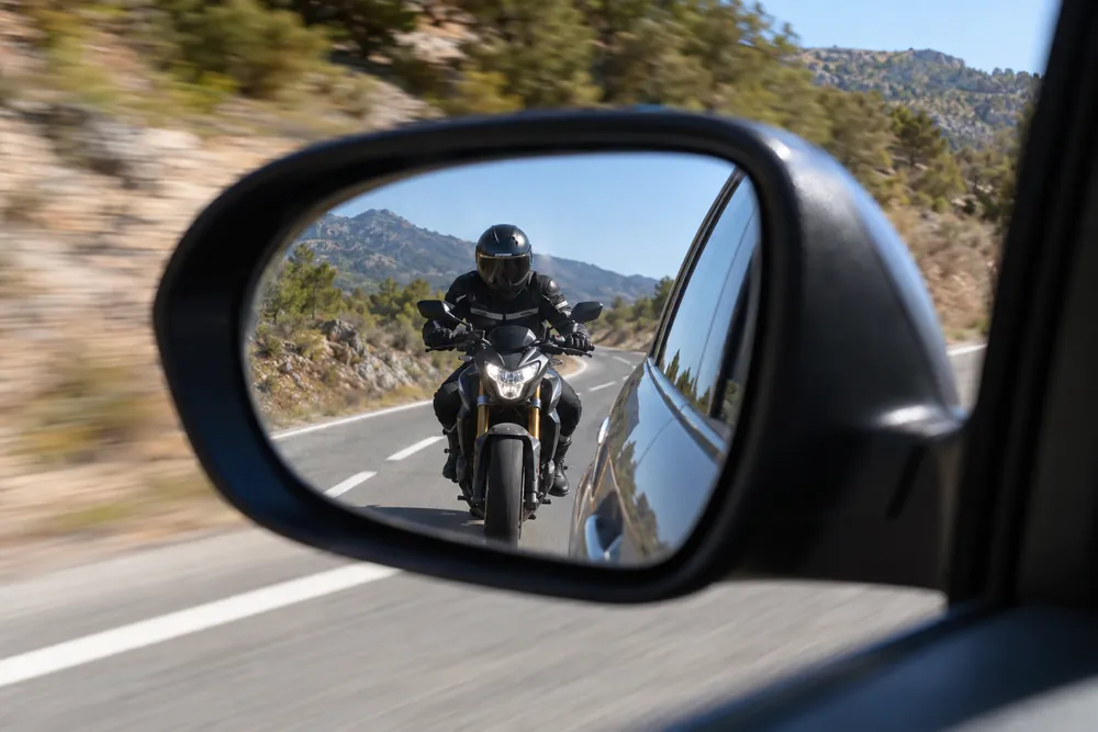 Motocicleta circulando muy pegada detrás, vista en el retrovisor exterior.
