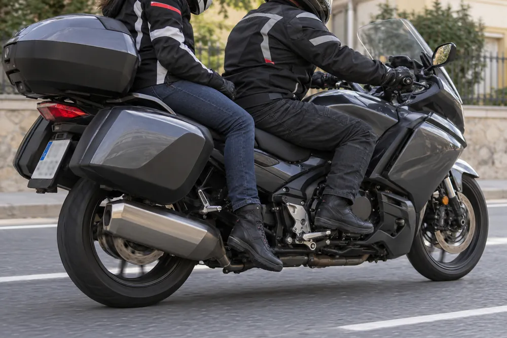 Pasajero de una motocicleta con los pies colgando por debajo de las estriberas.