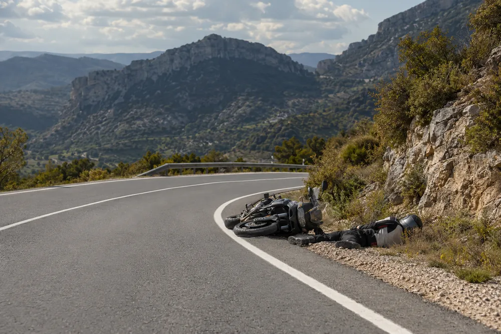 Motorista tendido en el arcén con el casco integral puesto, junto a su moto caída.