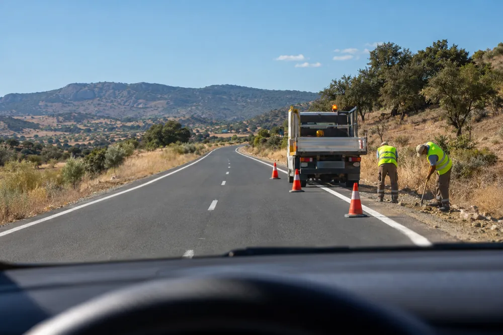 Operarios trabajando en el arcén junto a un camión de obra, vistos desde el coche que se acerca.