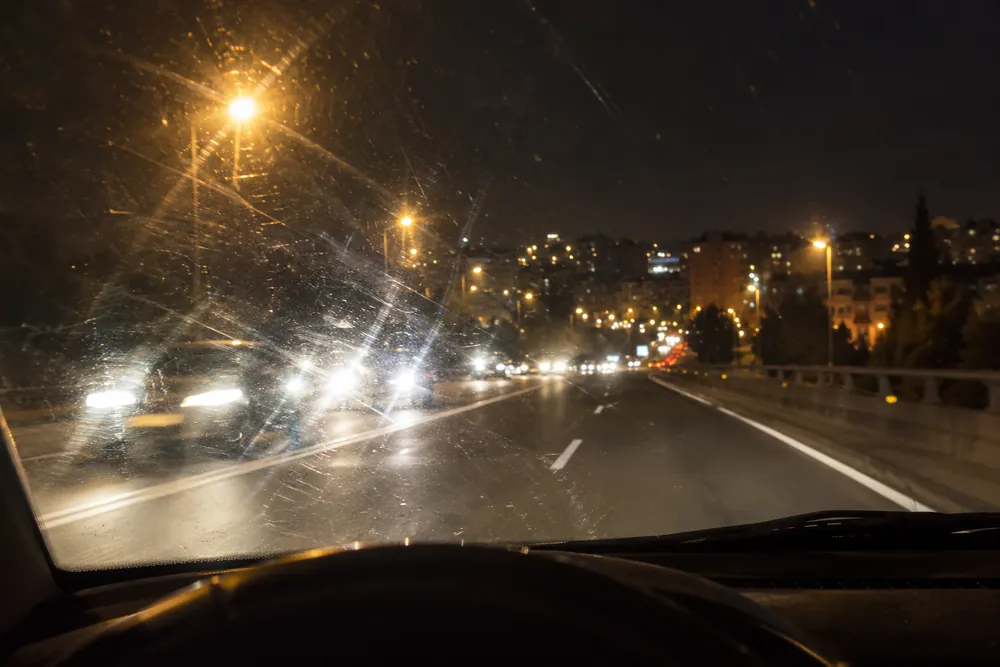Faros y farolas con halos vistos de noche a través de un parabrisas sucio.
